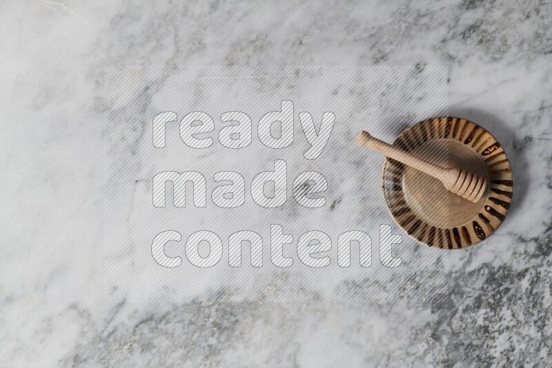 Multicolored pottery plate with wooden honey dipper in it on grey marble background