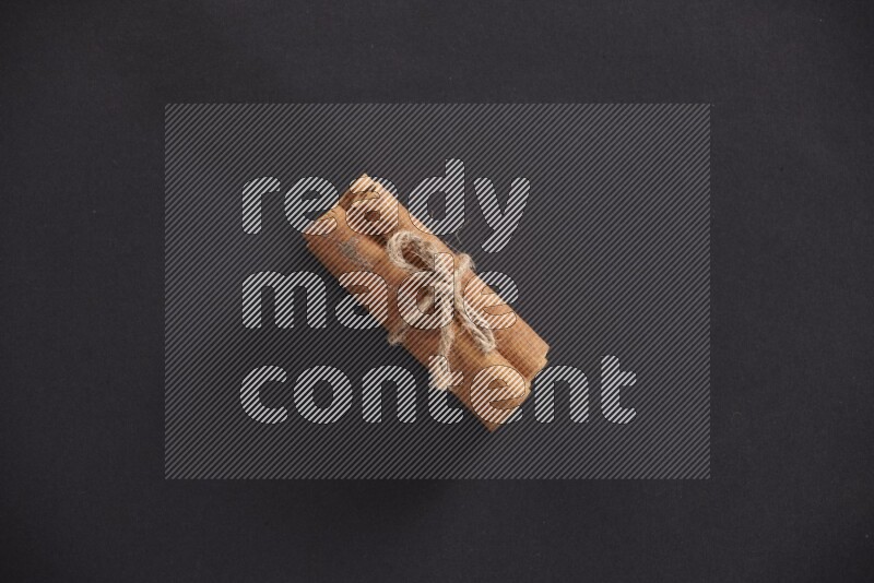 4 Cinnamon sticks stacked and bounded on black flooring
