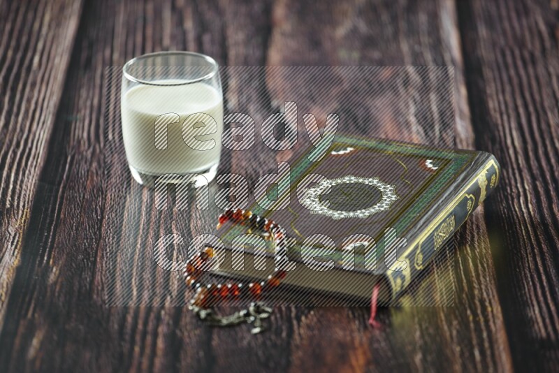Quran with dates, prayer beads and different drinks all placed on wooden background