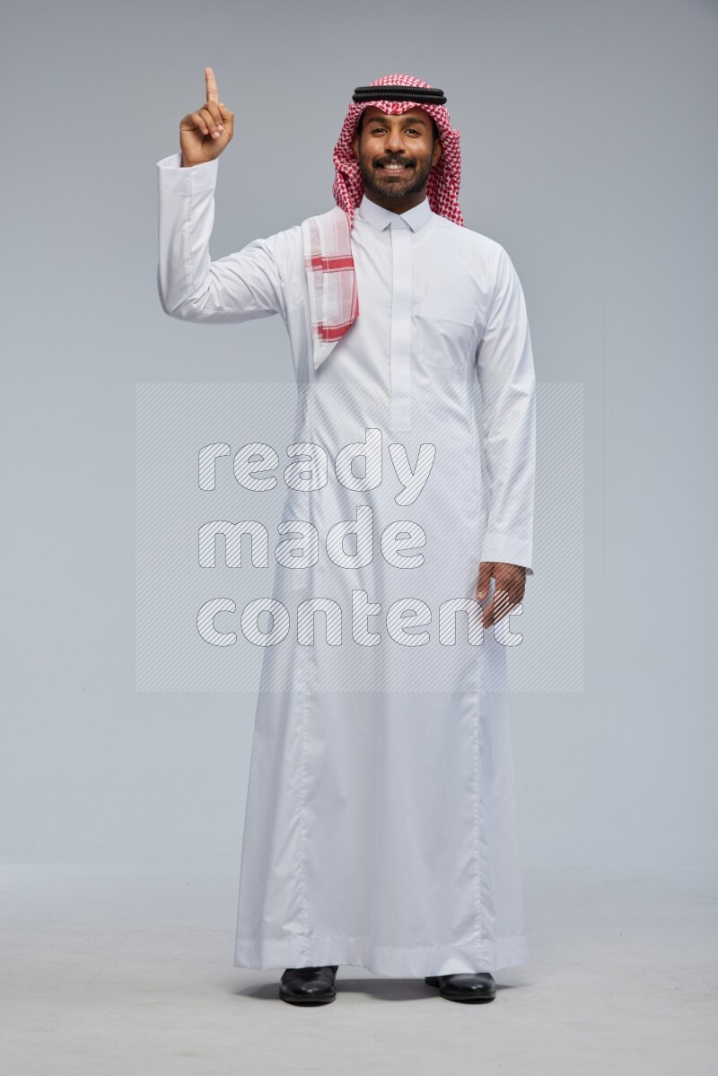 Saudi man Wearing Thob and shomag standing interacting with the camera on Gray background