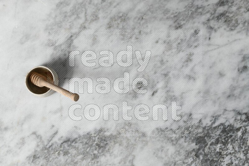 Black pottery bowl with wooden honey dipper in it on grey marble background