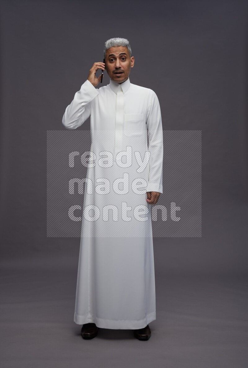 Saudi man wearing thob standing talking on phone on gray background