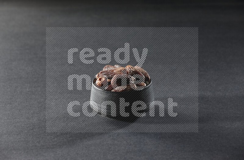 A black pottery bowl full of dried dates on a black background in different angles