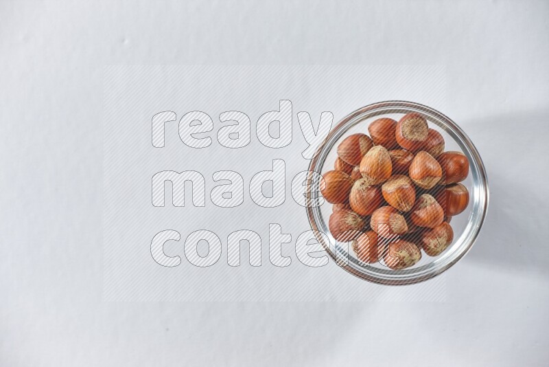 A glass bowl full of hazelnuts on a white background in different angles