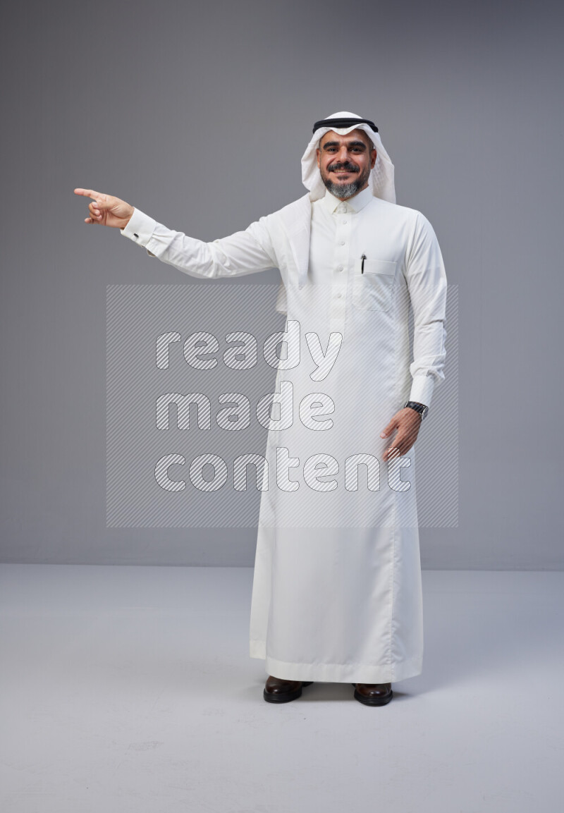 Saudi man Wearing Thob and white Shomag standing interacting with the camera on Gray background
