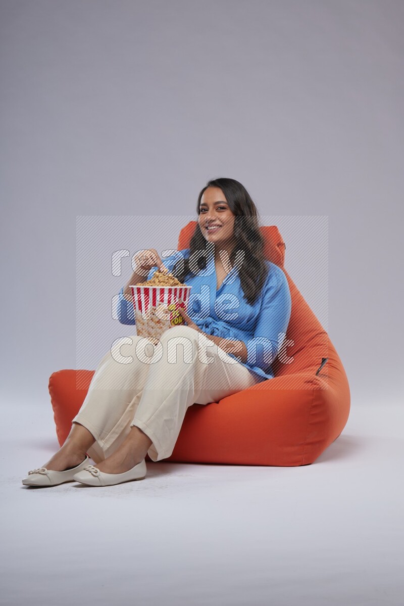 A woman sitting on an orange beanbag and eating popcorn
