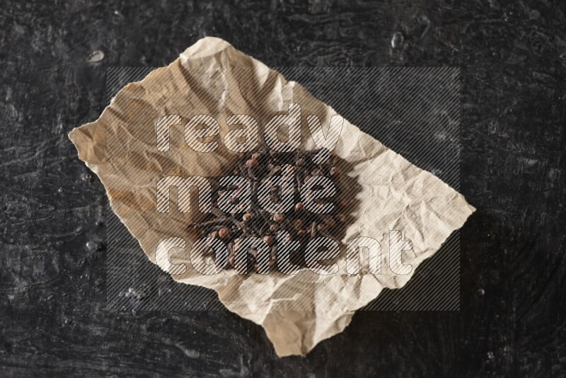 Cloves in crumpled piece of paper on a textured black flooring