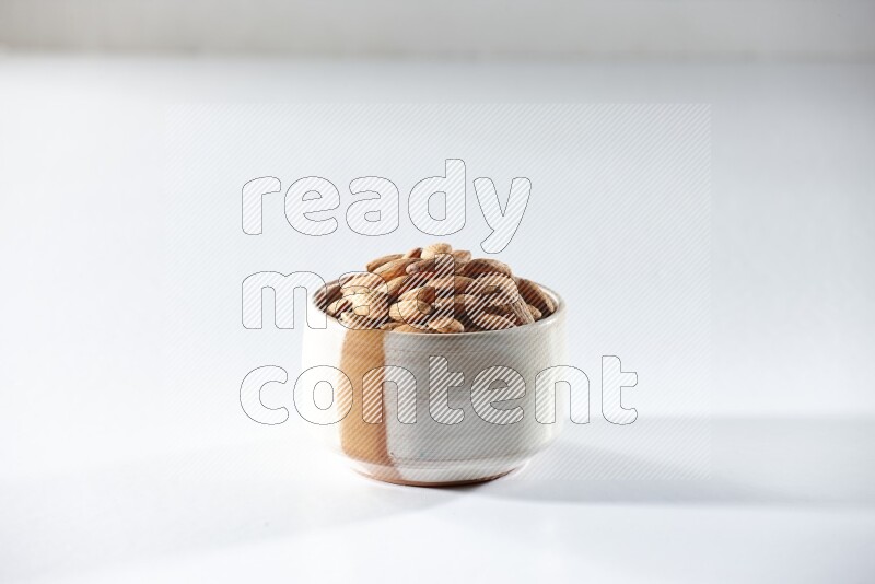 A beige ceramic bowl full of peeled almonds on a white background in different angles