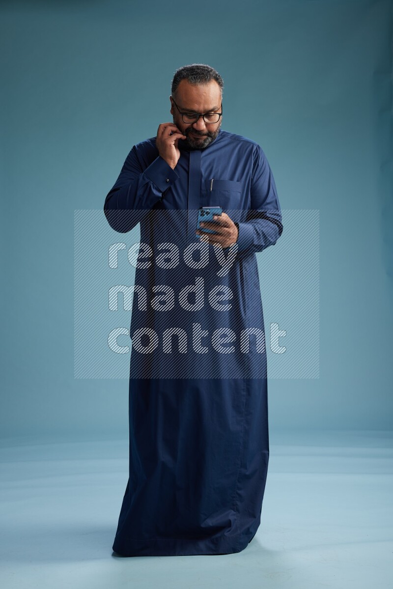 Saudi Man without shimag Standing texting on phone on blue background