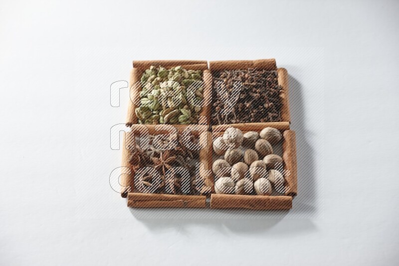 4 مربعات من أعواد القرفة ممتلئة بالهيل واليانسون والقرنفل وجوزة الطيب على أرضية بيضاء