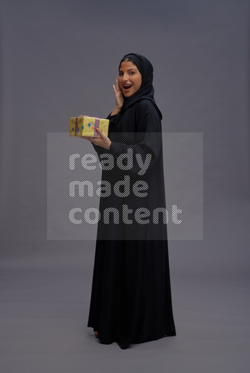 Saudi woman wearing Abaya standing holding gift box on gray background