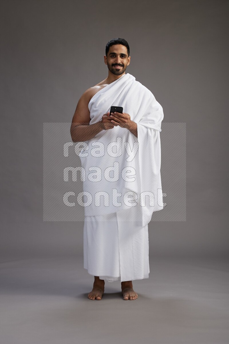 A man wearing Ehram Standing texting on phone on gray background