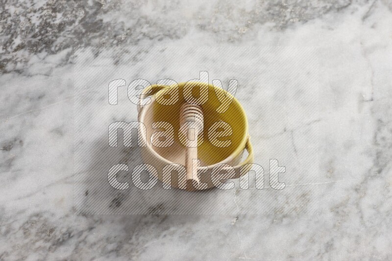 Multicolored pottery bowl with wooden honey dipper in it on grey marble background