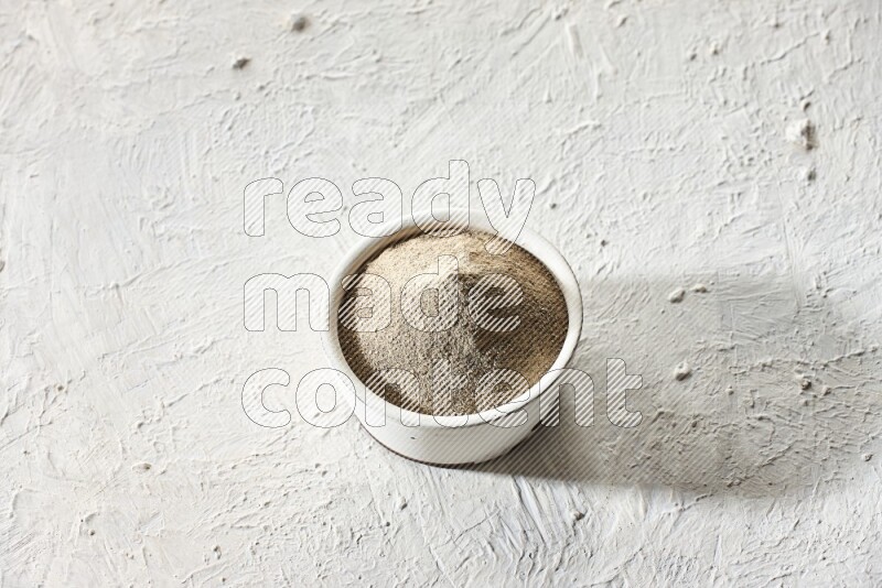 white pottery bowl full of white pepper powder on textured white flooring