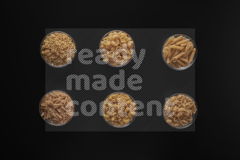 Different pasta types in 6 glass bowls on black background