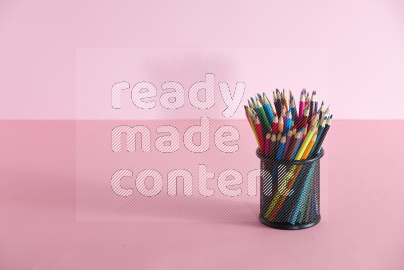 Pens, pencils and other different school supplies in a metal pen holder on rose background