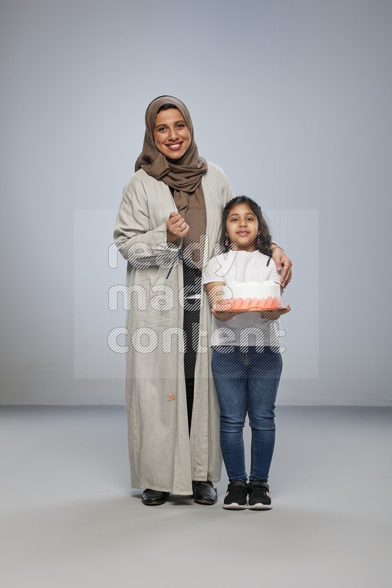 A girl giving a cake to her mother on gray background