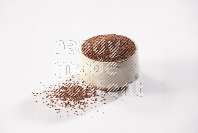 A beige pottery bowl full of garden cress seeds with more seeds spread on a white flooring