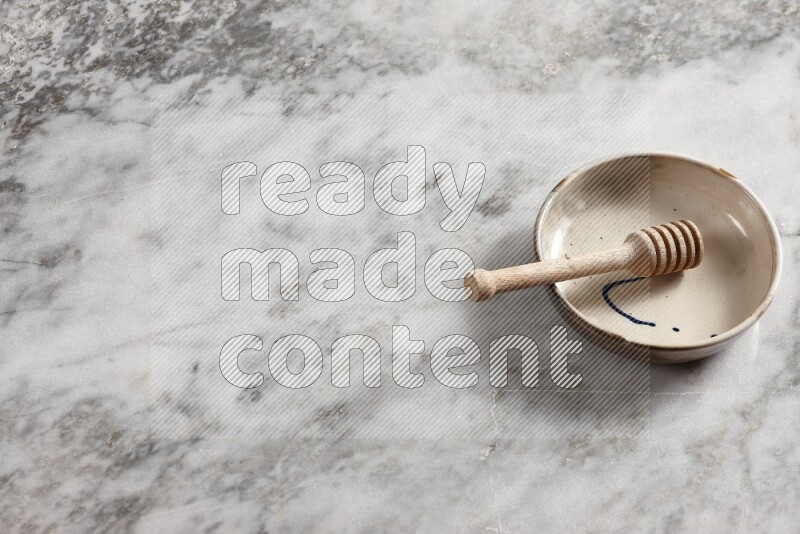 Multicolored pottery bowl with wooden honey dipper in it on grey marble background