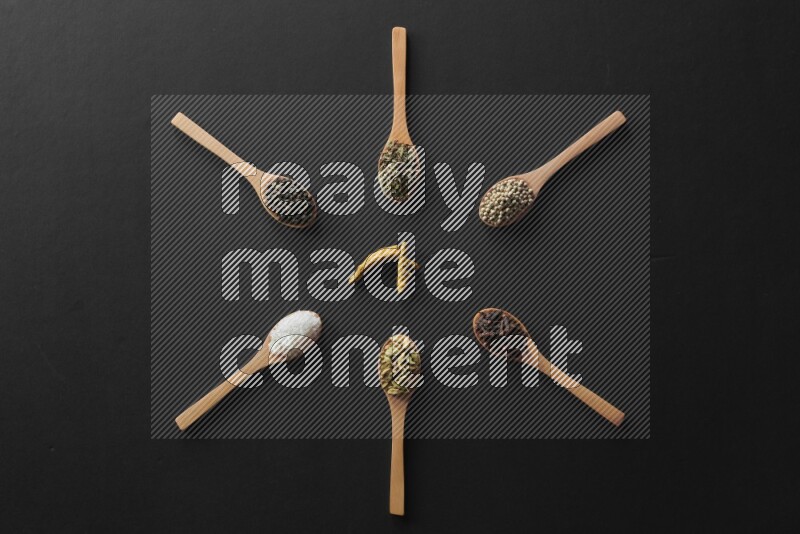 wooden spoons filled with white peppers, cloves, cardamom, salt, black peppers and basil on black flooring and shaped like a clock