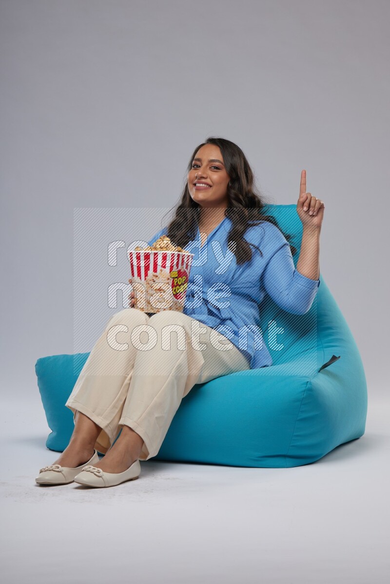 A woman sitting on a blue beanbag and eating popcorn