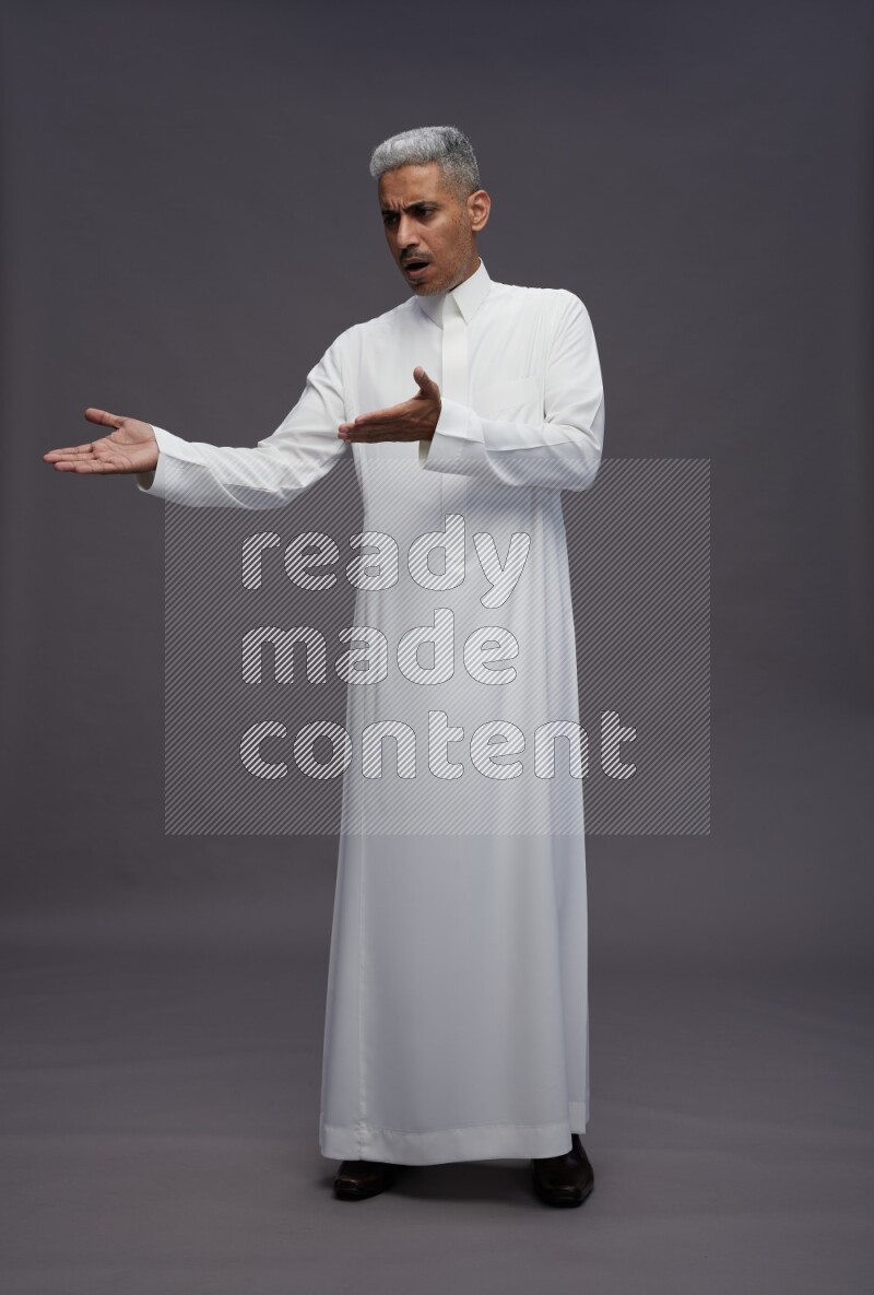 Saudi man wearing thob standing interacting with the camera on gray background