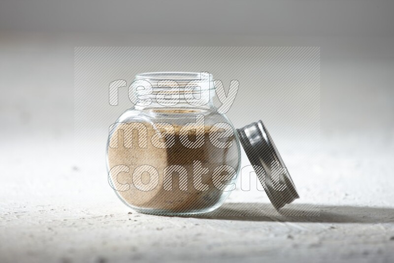 A glass spice jar full of cumin powder on textured white flooring