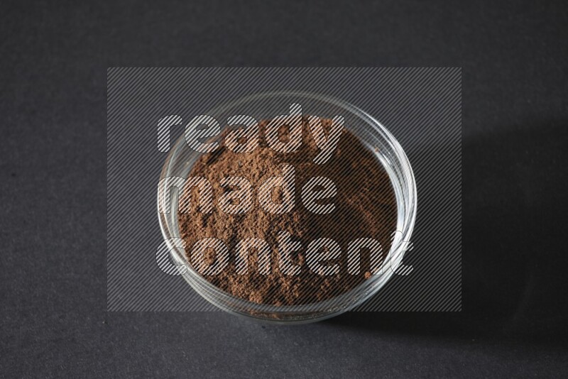 A glass bowl full of cloves powder on black flooring