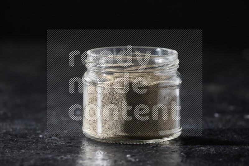 A glass jar full of white pepper powder on textured black flooring