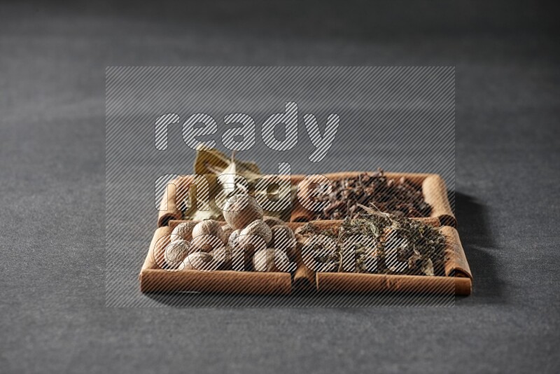 4 مربعات من عيدان القرفة ممتلئة بأوراق الغار والريحان المجفف والقرنفل وجوزة الطيب على أرضية سوداء