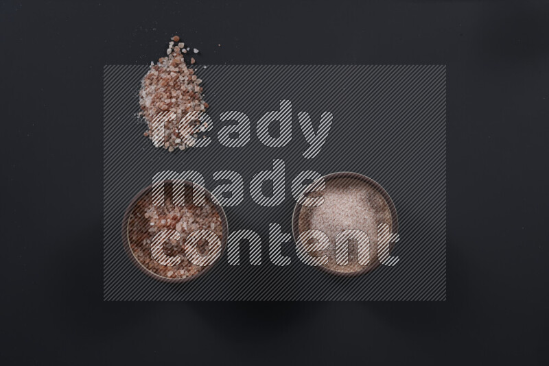 Pottery bowl full of fine himalayan salt and coarse himalayan salt on black background