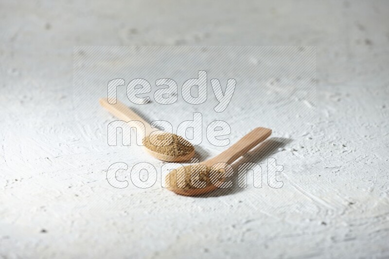 2 Wooden spoons full of cumin powder on a textured white flooring