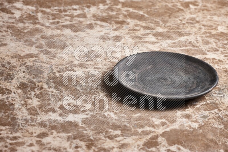 A circular black pottery plate on beige marble background