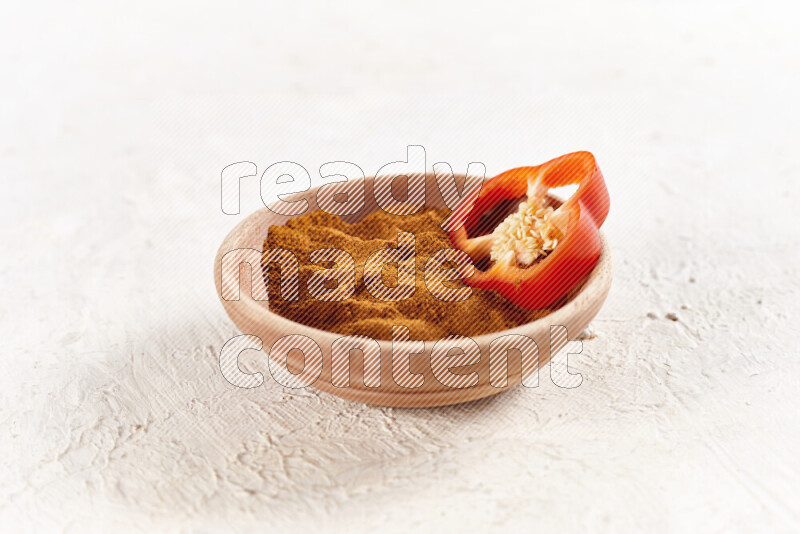A wooden bowl full of ground paprika powder on white background