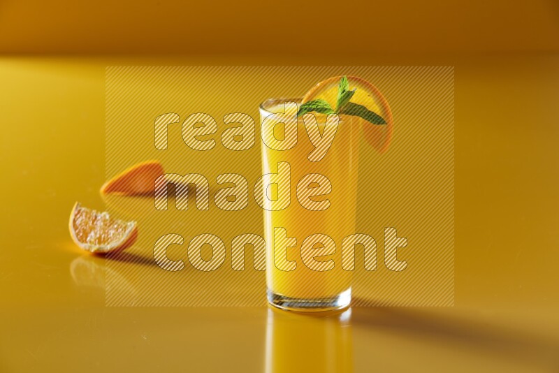 glass of orange juice with orange & mint  on yellow background