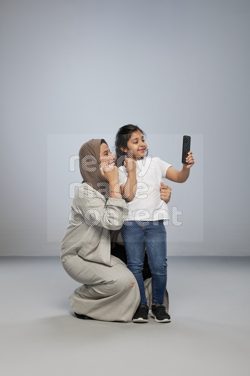 A girl standing taking selfie with her mother on gray background
