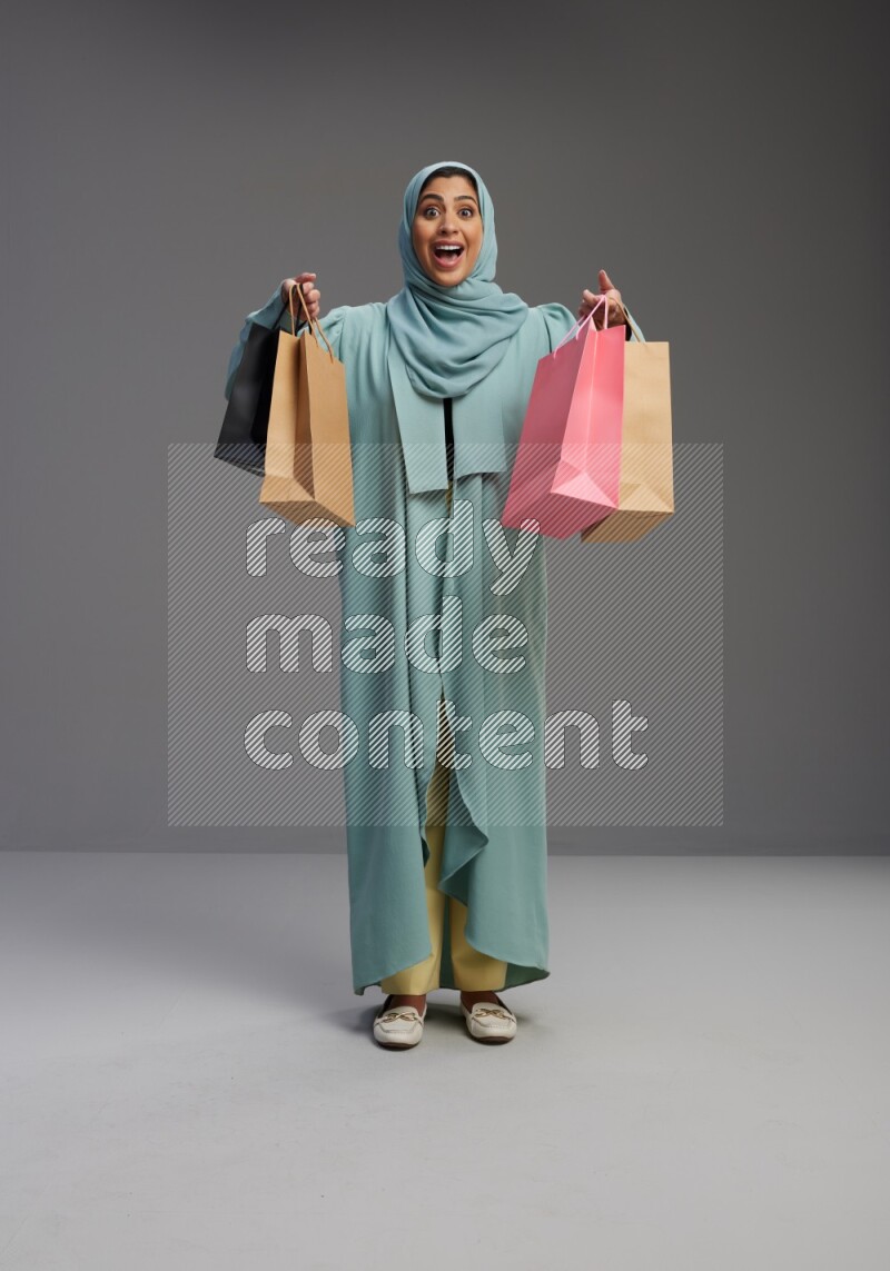 Saudi Woman wearing Abaya standing holding shopping bag on Gray background