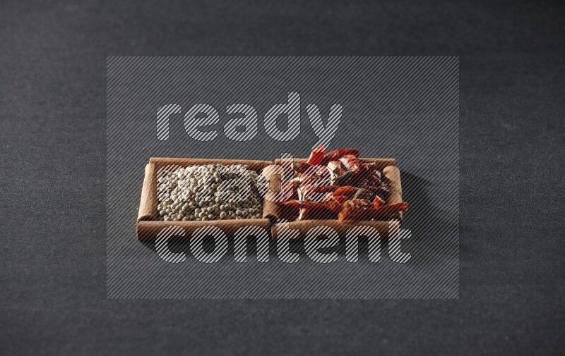 مربعان من أعواد القرفة ممتلئان بالفلفل الحار المجفف وحبوب الفلفل الأبيض علي خلفية سوداء