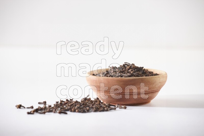 A wooden bowl full of cloves with spread grains on a white flooring
