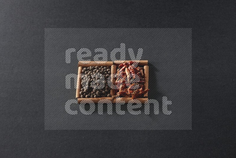 مربعان من أعواد القرفة ممتلئان بالفلفل الحار المجفف وحبوب بهار الفلفل الحلو علي خلفية سوداء