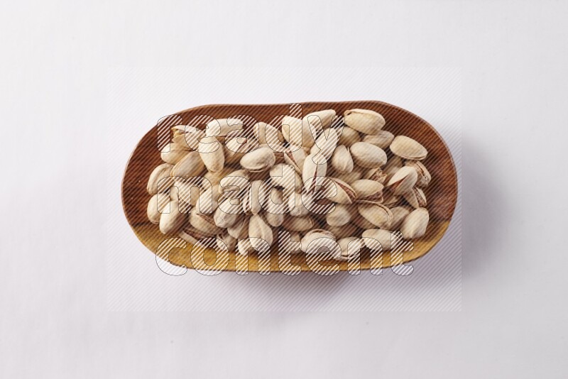 Pistachios in a wooden plate on white background