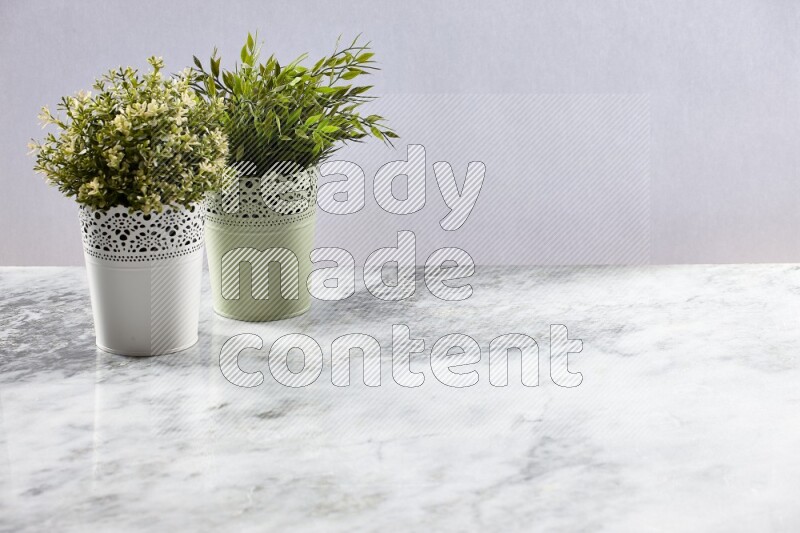 Two different artificial plants in white and green decorative pots on grey marble background