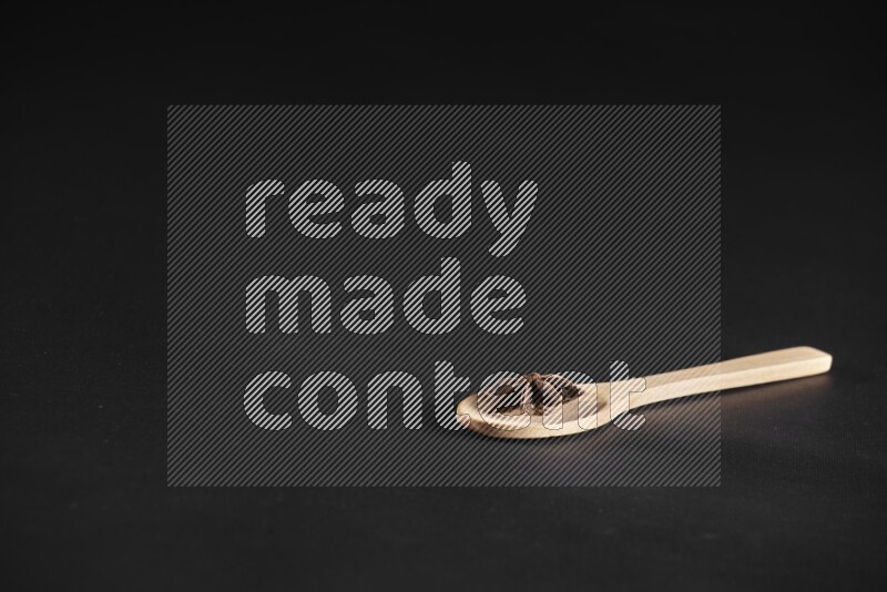 Star Anise in a wooden spoon on more stars anise filling the frame on black flooring