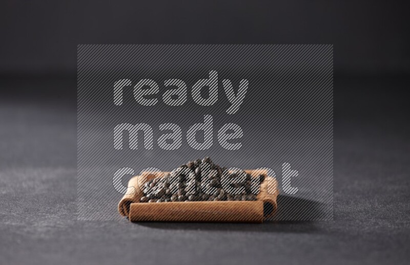 أربعة من أعواد القرفة مكونة شكل مربع بداخلها حبوب الفلفل الأسود علي خلفية سوداء