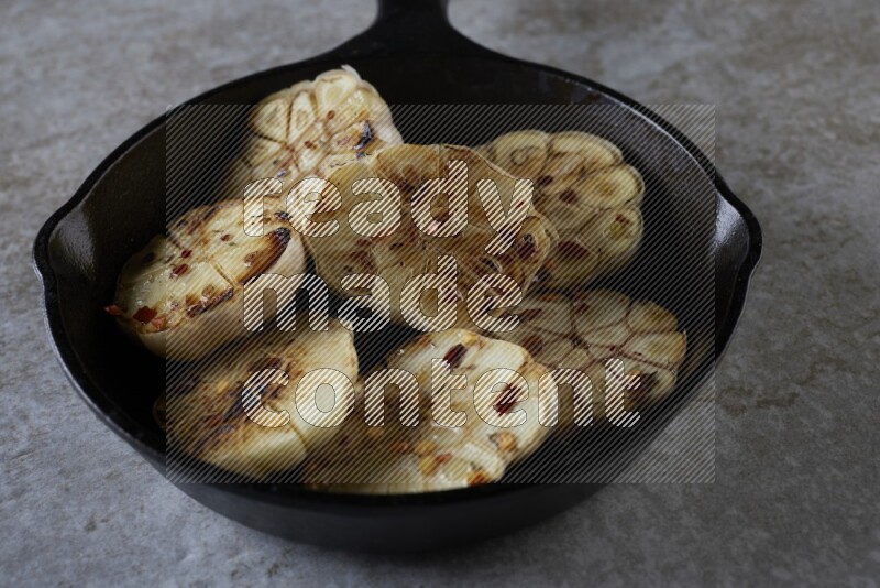 half's roasted garlic in a black pan on a grey textured countertop