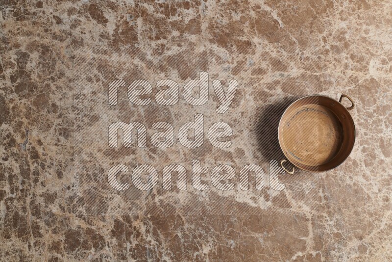 A small copper pan on beige marble background