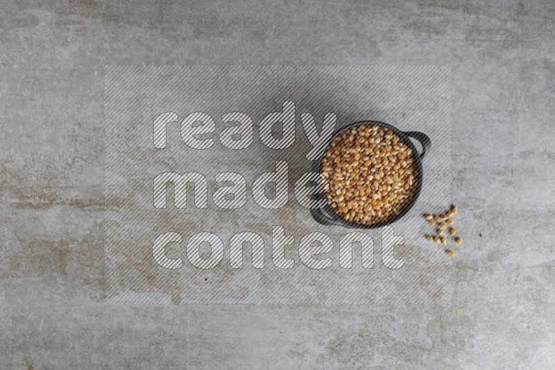 corn kernel in a black handheld ceramic bowl on a grey textured countertop