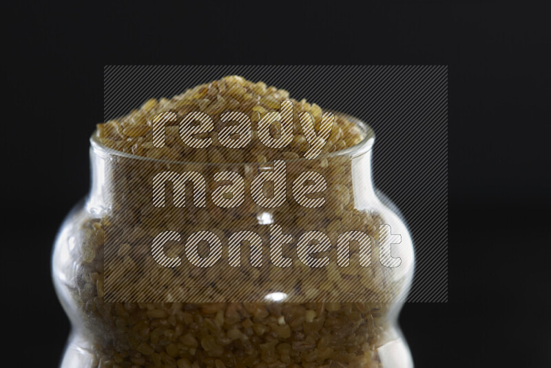 Coarse bulgur in a glass jar on black background