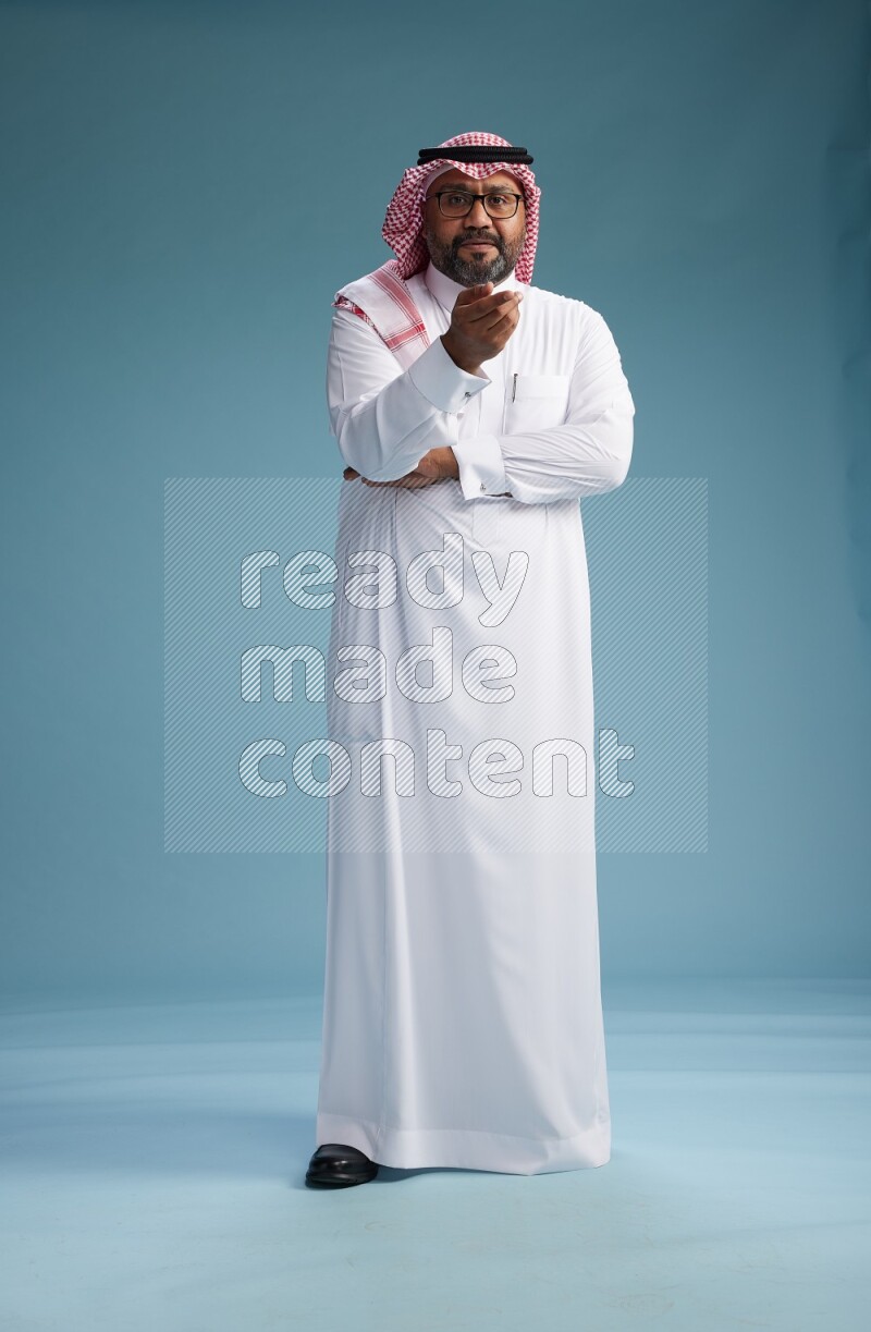 Saudi Man with shimag Standing Interacting with the camera on blue background