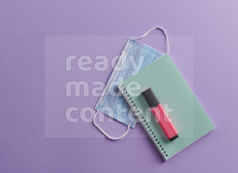 A blue notebook with school supplies on purple background